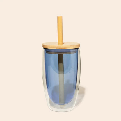 Blue double walled glass tumbler with a bamboo lid and straw on a beige background