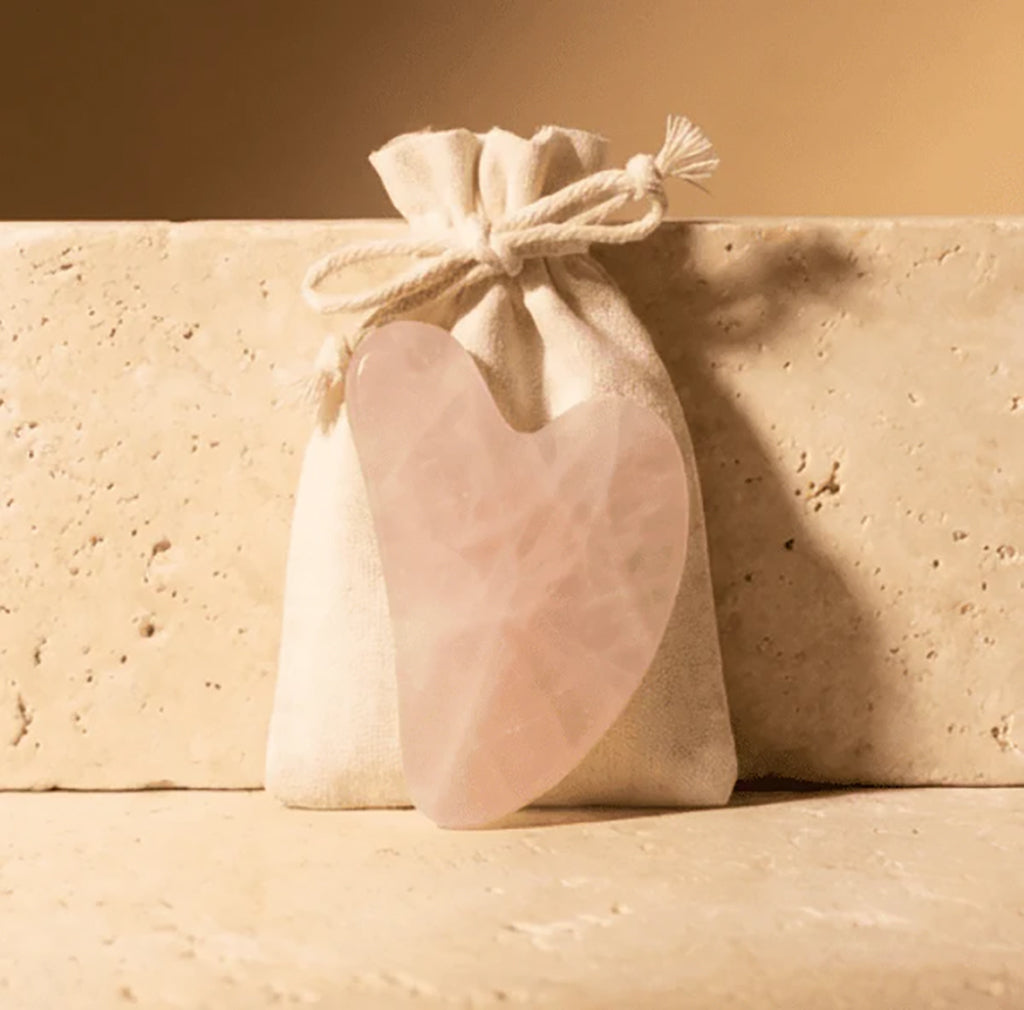 Rose Quartz Gua Sha stone in a beige drawstring bag on a beige surface