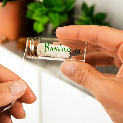 Person holding a small glass container of bamboo floss with greenery in the background.