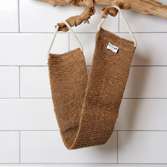 Sisal Back Scrubber with bamboo handles hanging on a wooden branch against a white tiled wall.
