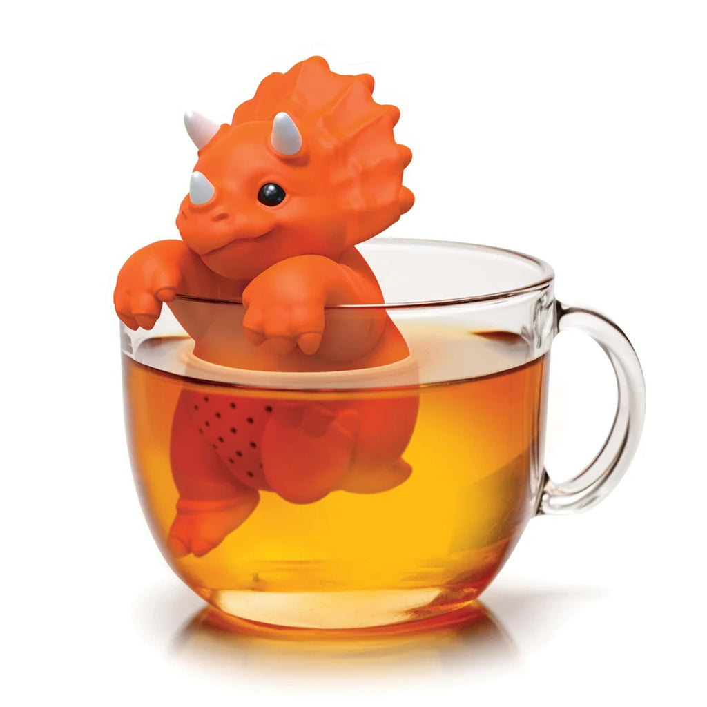 An orange dinosaur-shaped tea infuser resting inside a clear glass teacup filled with tea, shown on a clean white background.